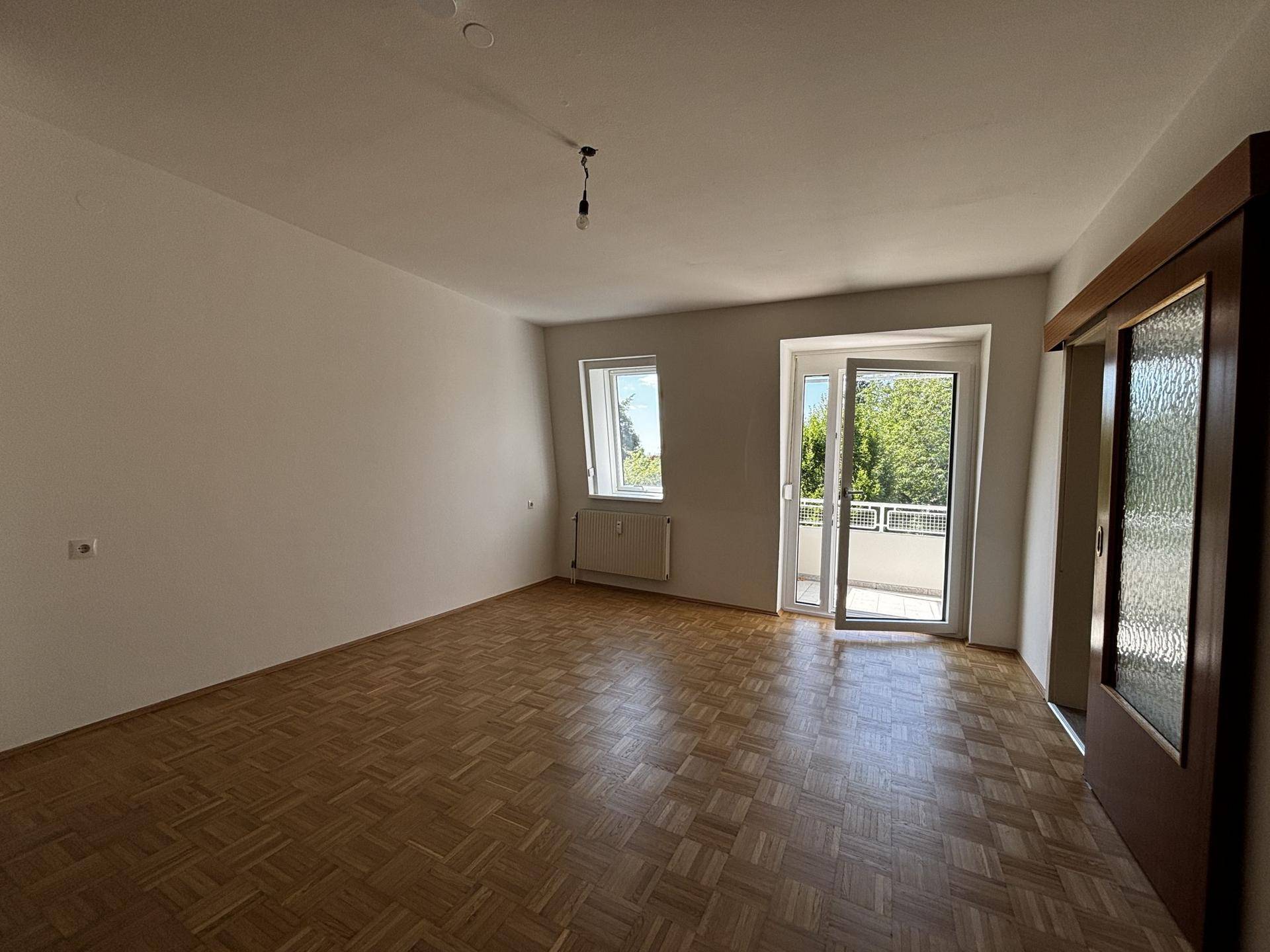 Helles Wohnzimmer mit Parkettboden, Fenster und direktem Zugang zu einem Balkon.