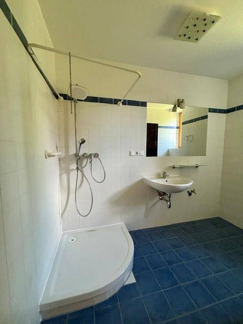 Badezimmer mit Duschkabine, Waschbecken und Spiegel, ausgestattet mit blauen Bodenfliesen.