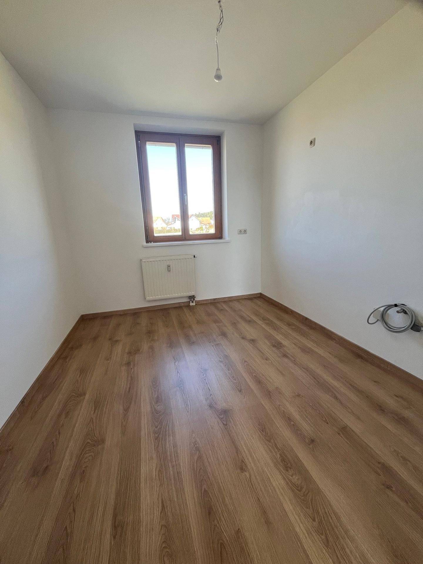 Helles Zimmer mit Laminatboden, Fenster und Heizkörper, geeignet als Kinder- oder Gästezimmer.