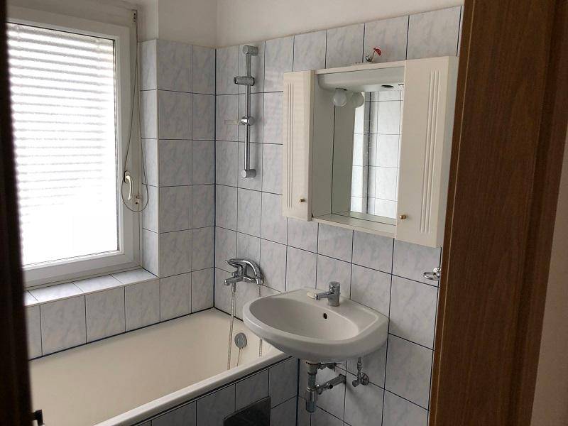 Helles Badezimmer mit Badewanne, Waschbecken, Spiegelschrank und Fenster.