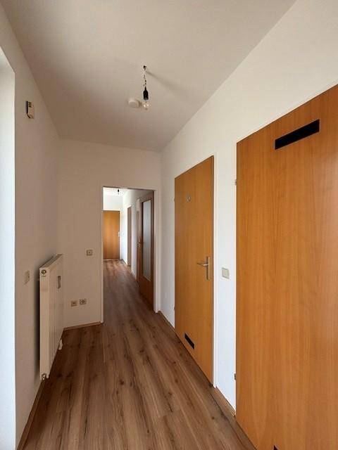 Heller Flur mit Laminatboden und mehreren Holztüren, der zu verschiedenen Räumen führt.