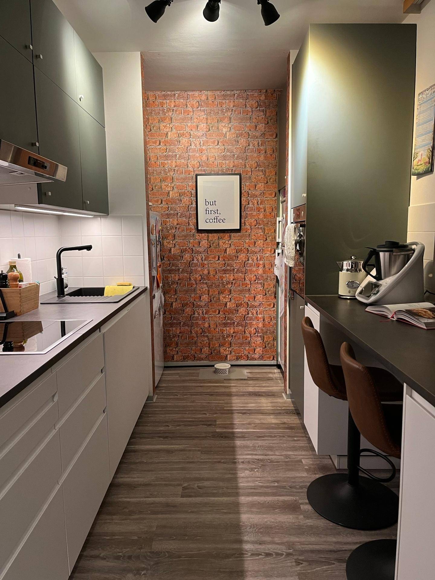 Moderne Küche mit dunkelgrünen Oberschränken, Backsteinwand und kleiner Frühstücksbar.