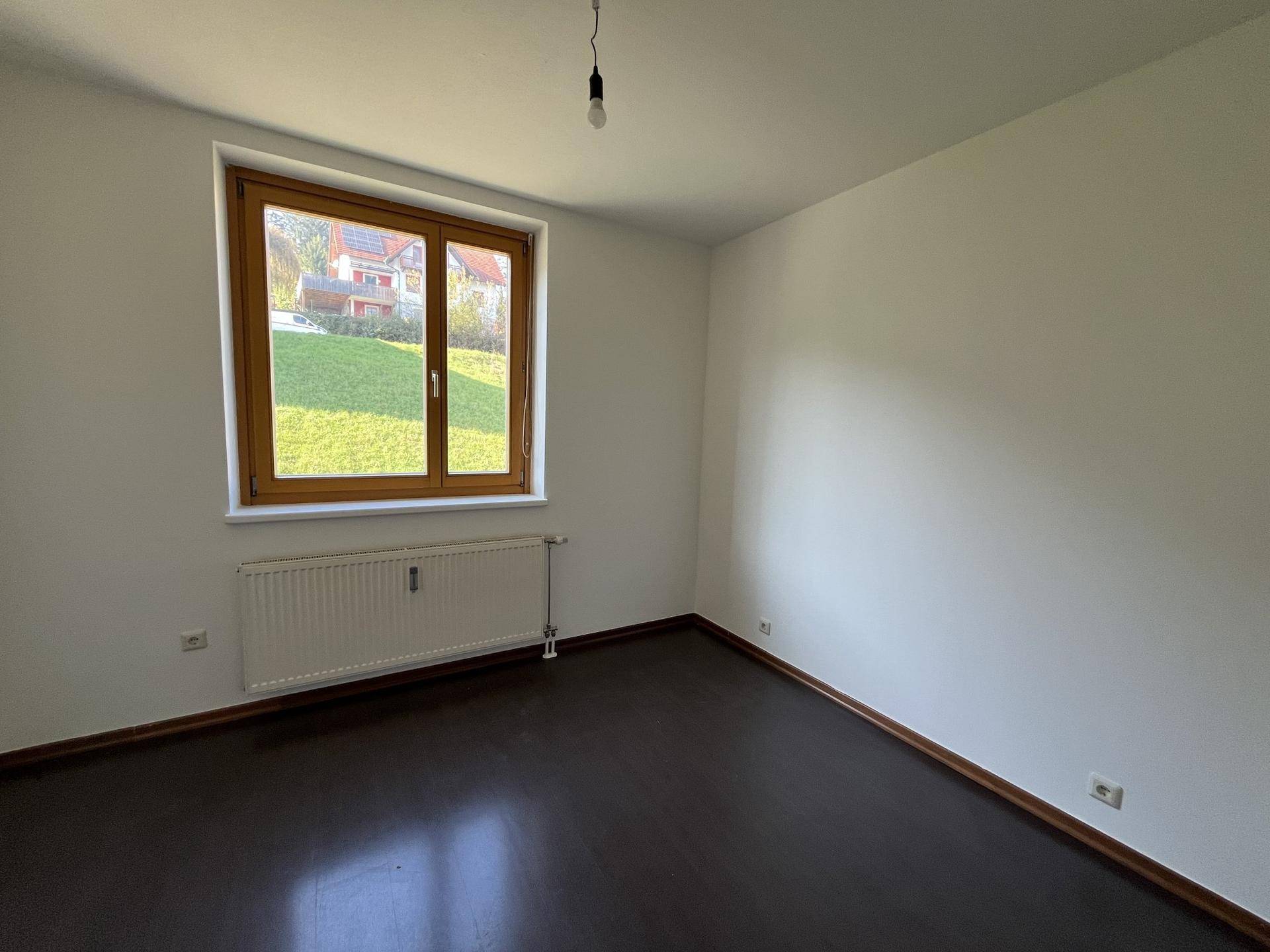 Gemütliches Schlafzimmer mit dunklem Parkettboden und großem Fenster, das den Raum erhellt.