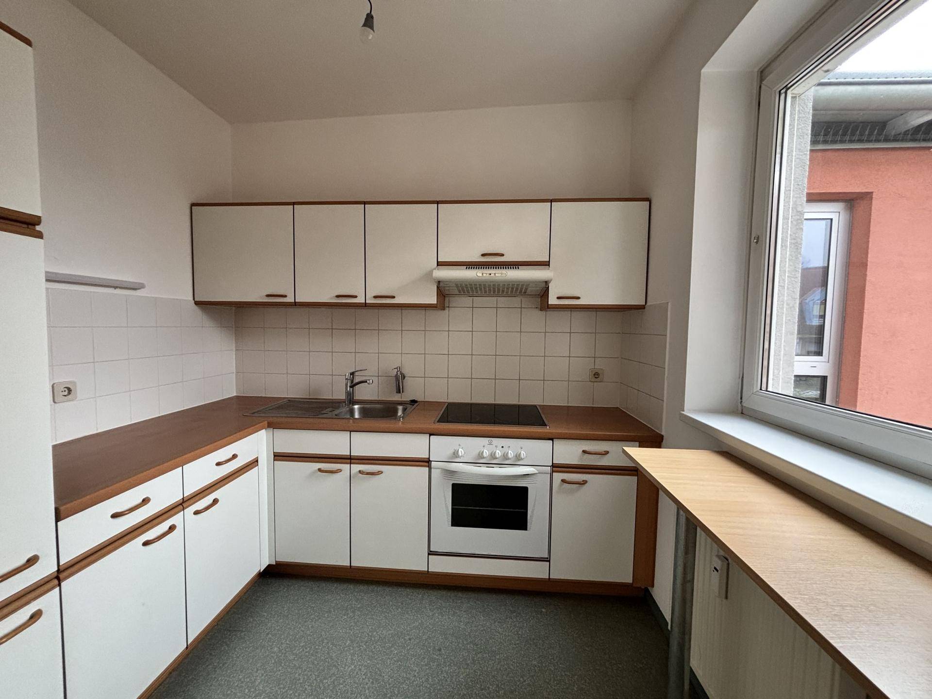 Helle Küche mit Fenster, weißen Schränken, Holzarbeitsplatte und Kochfeld.