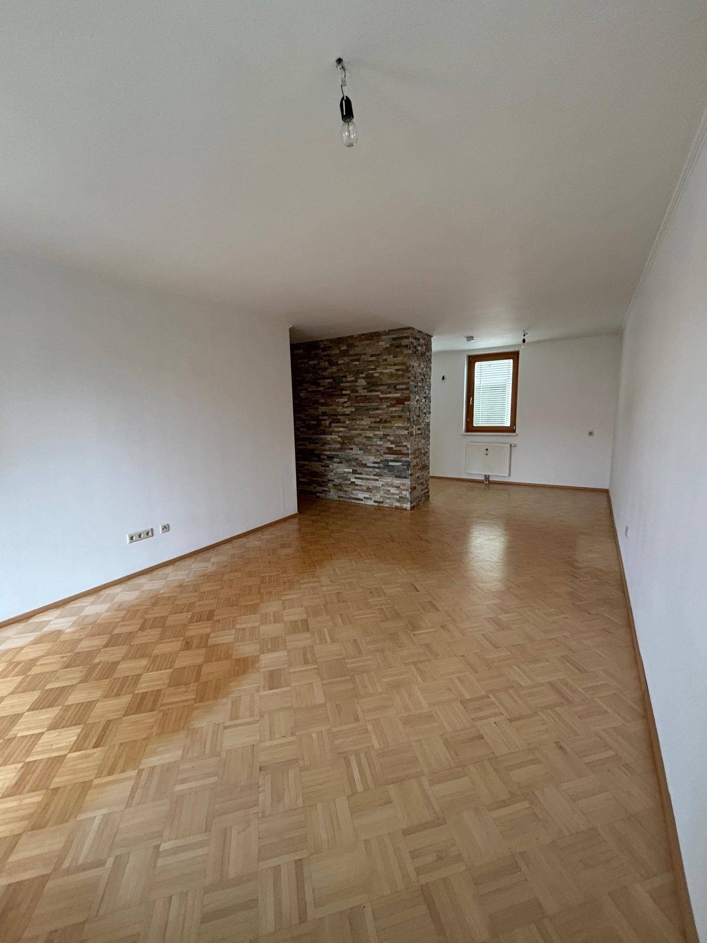 Geräumiges Wohnzimmer mit Parkettboden und einer dekorativen Steinwand als Akzent.