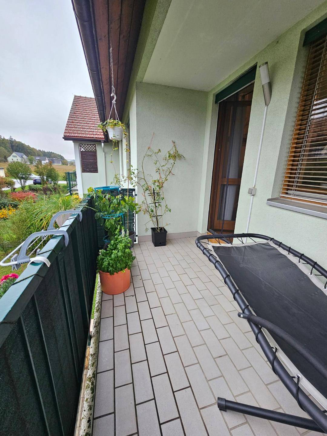 Langer Balkon mit Fliesenboden, Pflanzen und Blick auf die Umgebung.