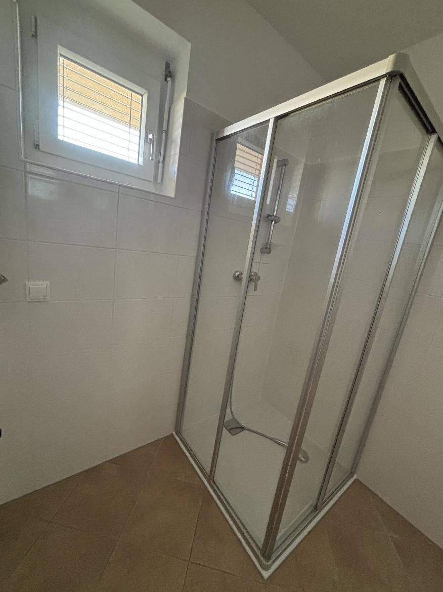 Badezimmer mit Duschkabine, weißen Fliesen und kleinem Fenster für Tageslicht.