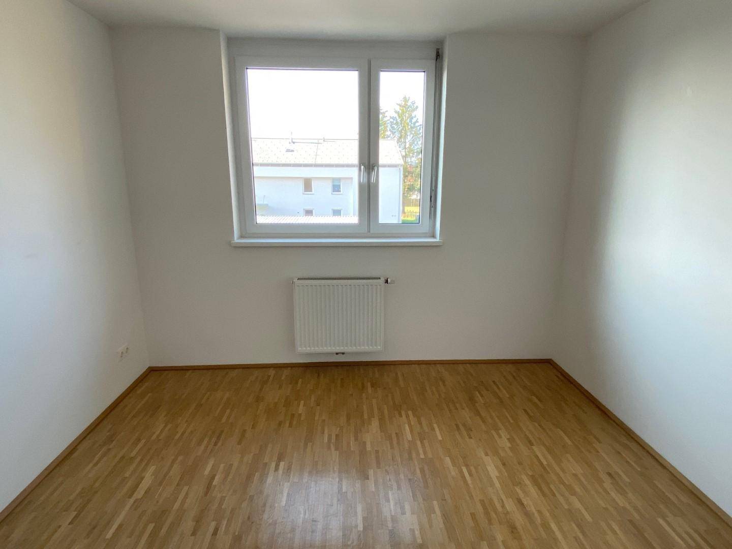 Helles Zimmer mit Parkettboden und einem großen Fenster, ideal als Schlaf- oder Kinderzimmer.