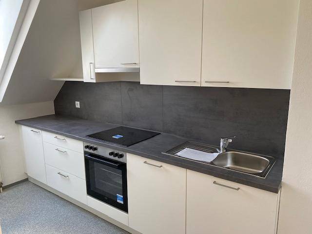 Moderne Einbauküche mit weißen Schränken, dunkler Arbeitsplatte und integrierten Geräten unter Dachschräge.