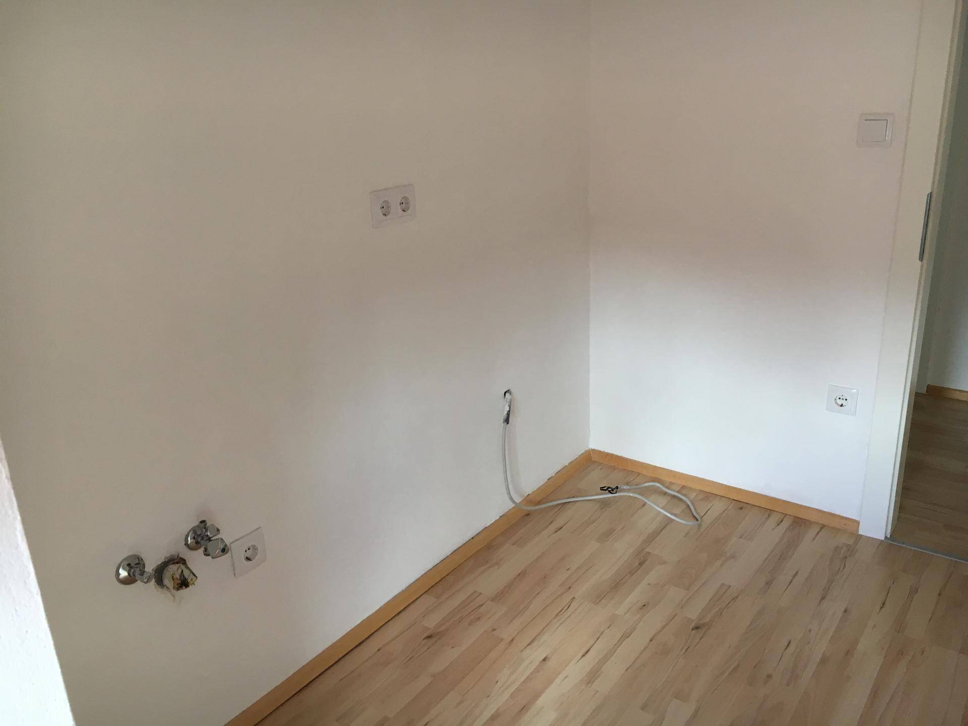 Leerer Raum mit Anschlüssen für eine Küche und hellem Holzfußboden.