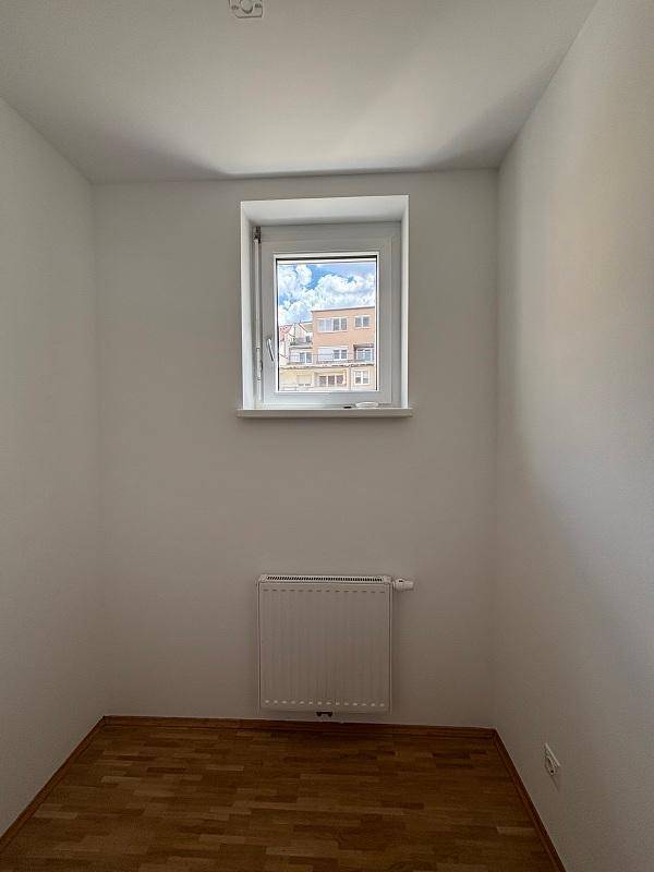 Helles Zimmer mit Parkettboden, Heizkörper und einem Fenster mit Blick nach draußen.