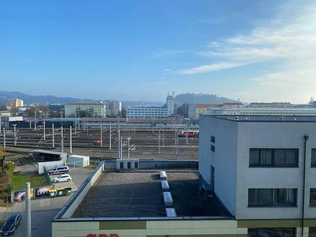 Weitblick über Dächer, Bahngleise und die städtische Umgebung mit Bergen am Horizont.