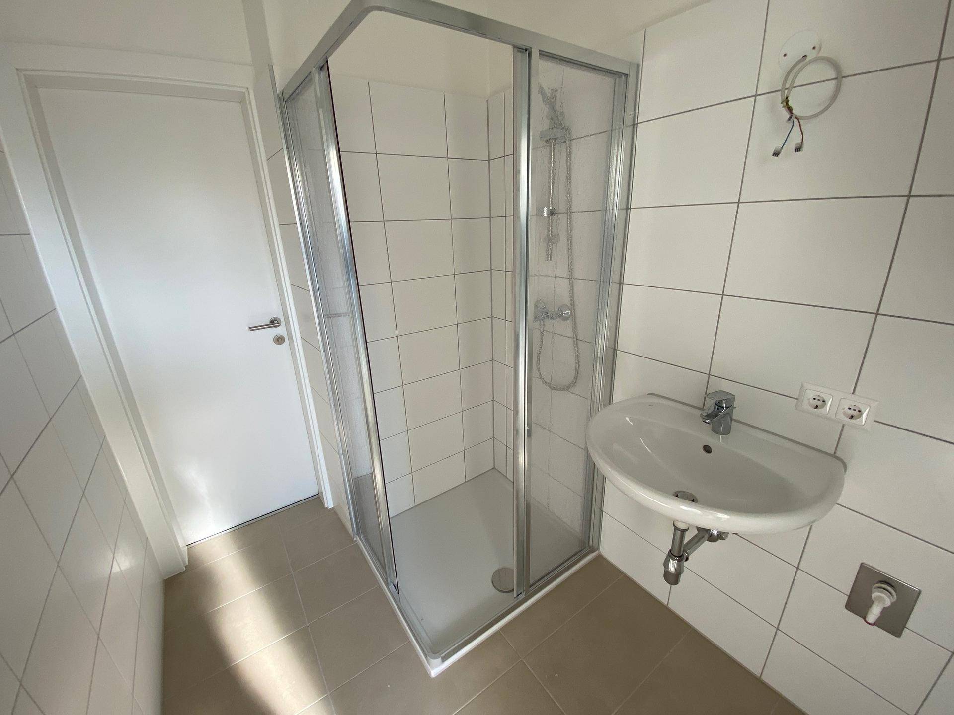 Helles Badezimmer mit Duschkabine, Waschbecken und weißen Fliesen.