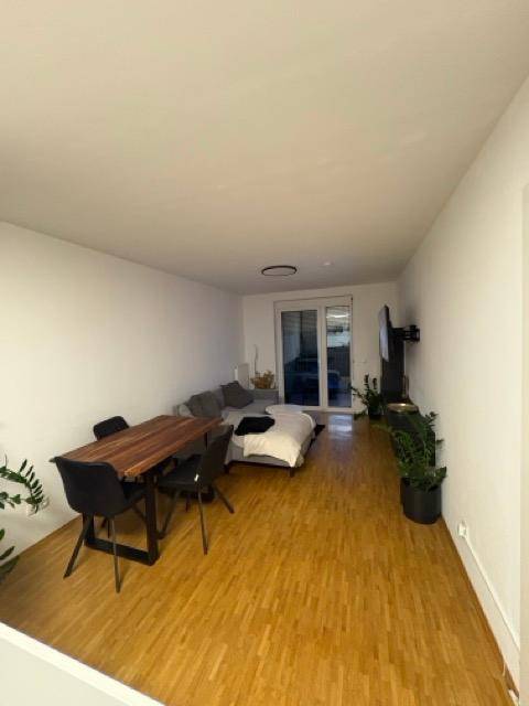 Offener Wohn- und Essbereich mit Holztisch, Sofa und Zugang zum Balkon.