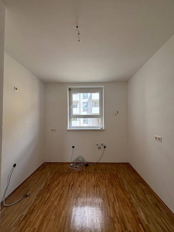 Leeres Zimmer mit Parkettboden und einem Fenster, das viel Tageslicht in den Raum lässt.