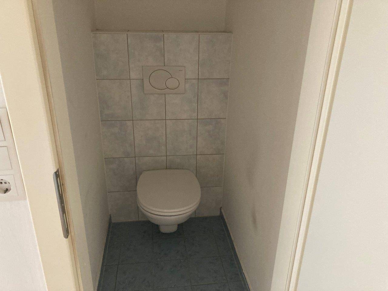 Kleines Gäste-WC mit Wand-WC und hellblauen Fliesen an Wand und Boden in Standardausführung.