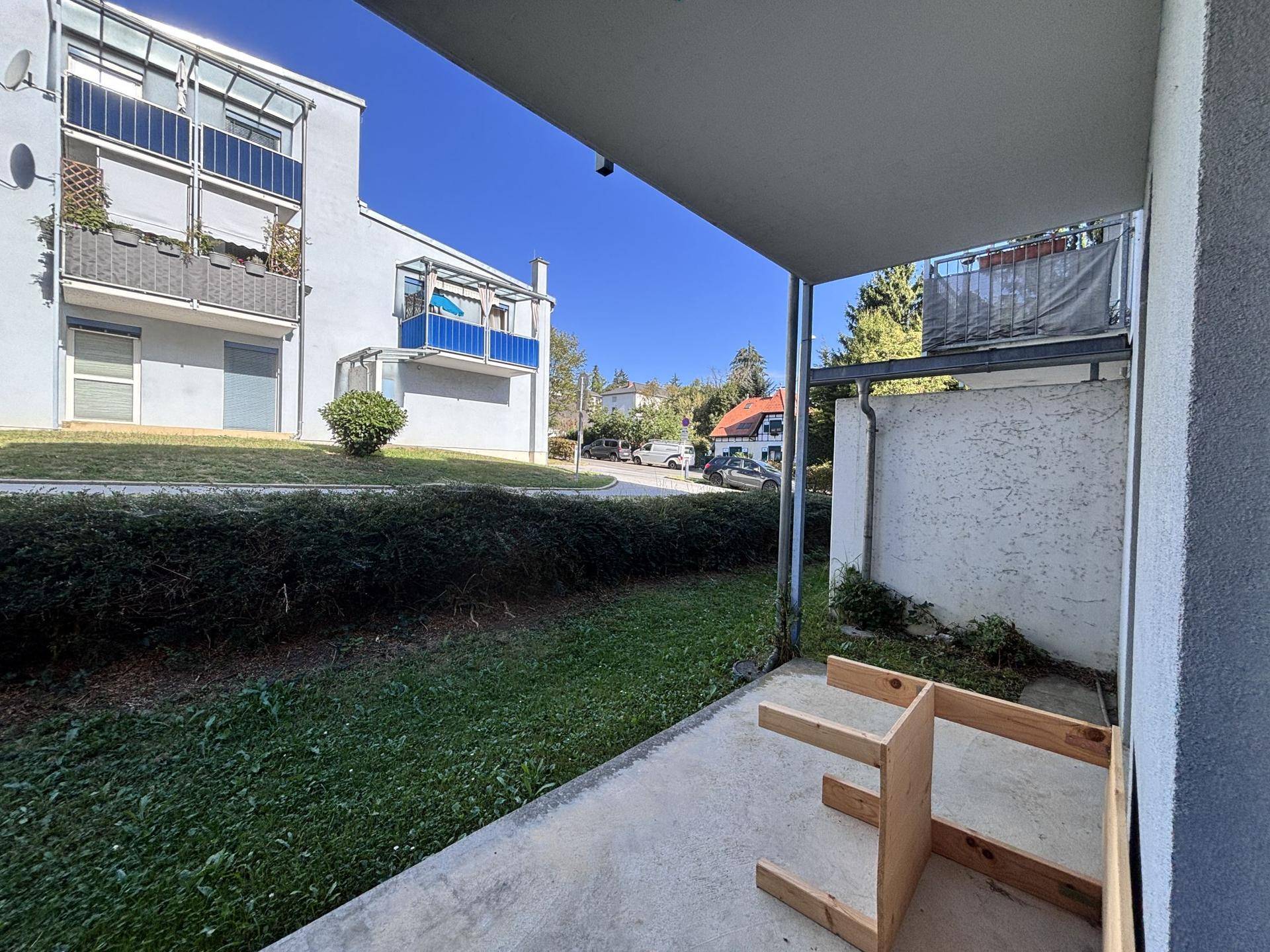 Überdachte Terrasse mit Blick auf den Garten und angrenzende Gebäude.