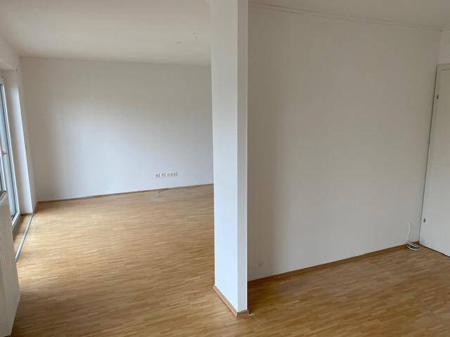 Heller Wohnraum mit Parkettboden und einem tragenden Pfeiler in der Mitte des Zimmers.