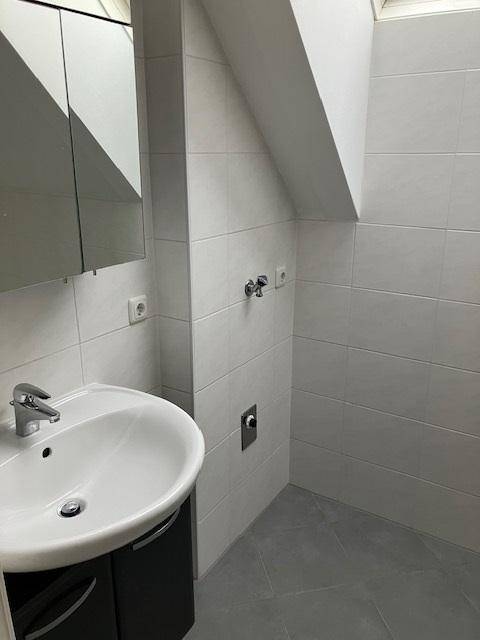 Badezimmer mit Waschbecken, Spiegelschrank und weißen Fliesen unter einer Dachschräge.
