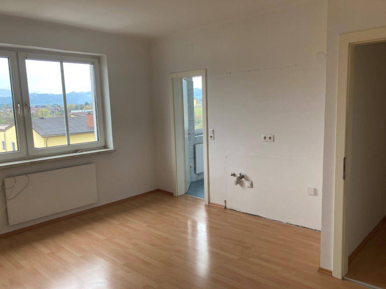 Heller Raum mit Laminatboden, Fenster und Anschlüssen für eine zukünftige Küche oder Bad.