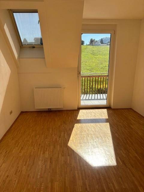 Lichtdurchflutetes Dachgeschosszimmer mit Parkettboden, Dachfenster und Zugang zu einem kleinen Balkon.
