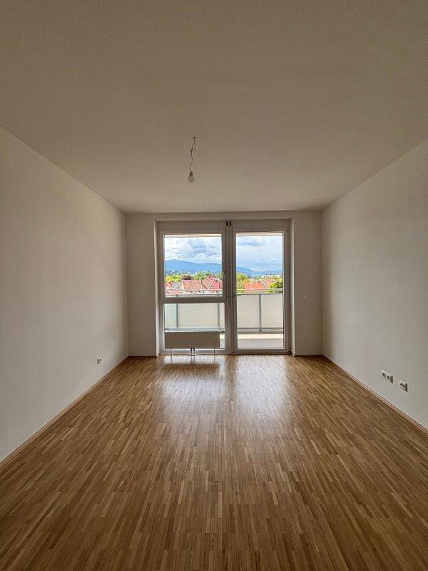 Geräumiges Wohnzimmer mit Parkettboden, Balkonzugang und weitem Blick auf die Landschaft und Berge.