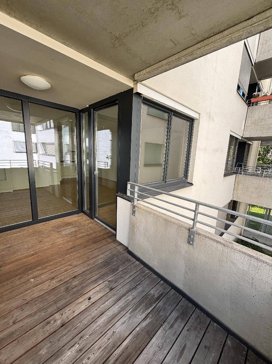 Heller Balkon mit Holzfußboden und großem Glaszugang zum Innenbereich der Wohnung.