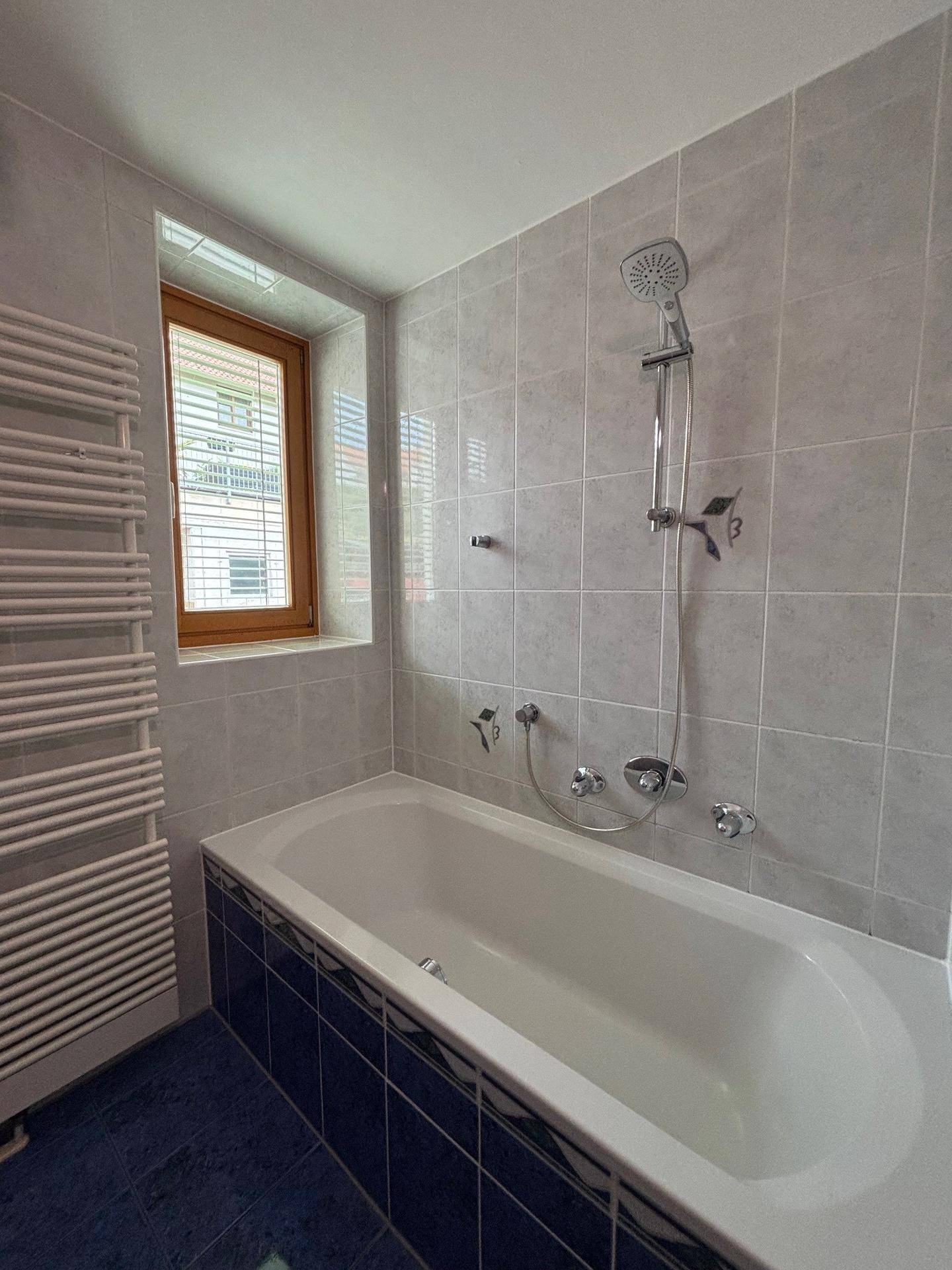 Badezimmer mit Badewanne, Duschvorrichtung, Fliesenwänden und einem beheizten Handtuchhalter.