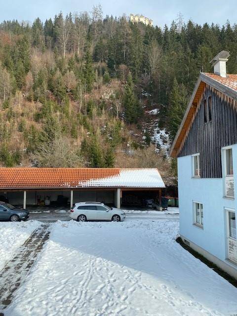 Verschneite Umgebung mit bewaldeten Hügeln und einem Carport im Vordergrund.