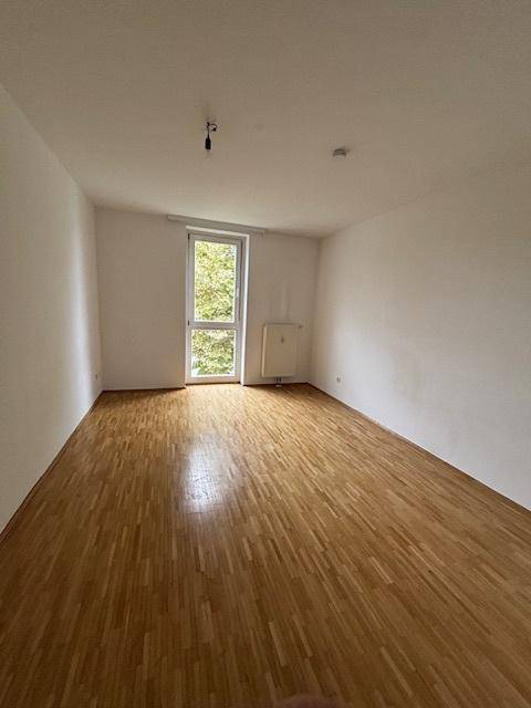 Heller Raum mit Holzparkett und großem Fenster, das eine angenehme Atmosphäre schafft.