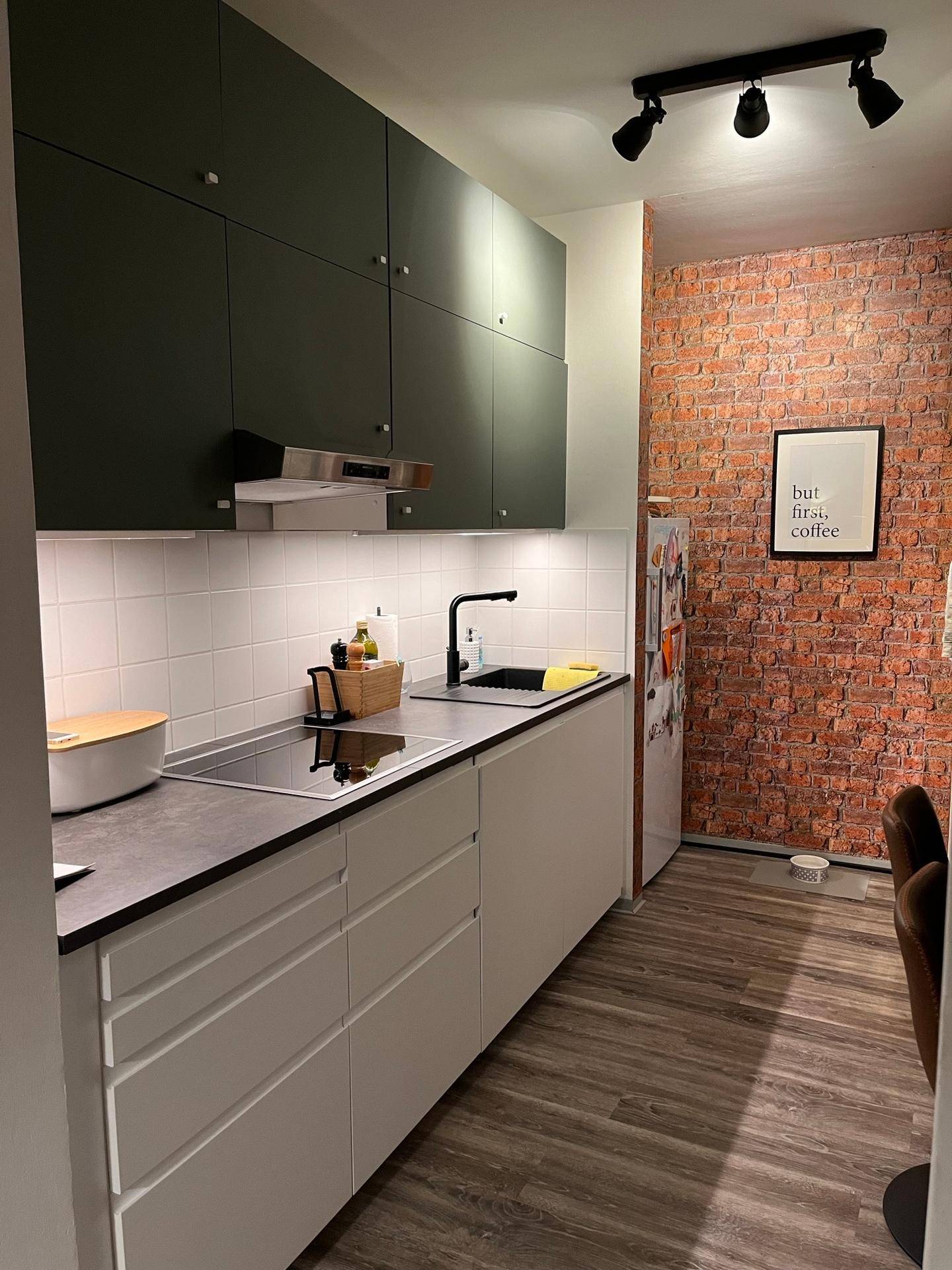 Helle Küche mit modernen Schränken, Induktionskochfeld und dekorativer Backsteinwand.