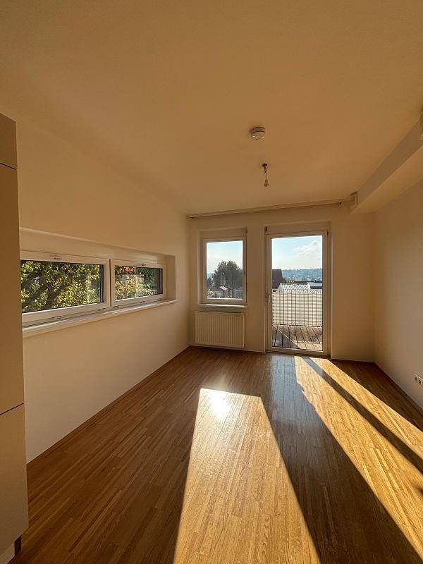 Heller Raum mit Holzboden und Zugang zum Balkon, bietet viel Tageslicht und Ausblick.