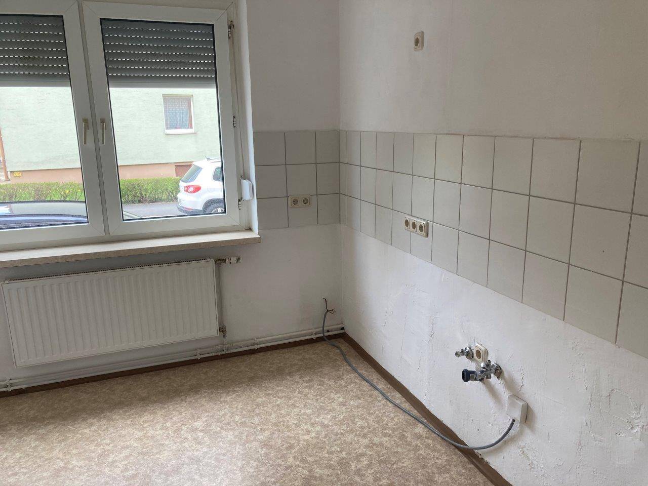 Leere Küche mit Fliesenwand, Fenster und Anschlüssen für Küchengeräte.