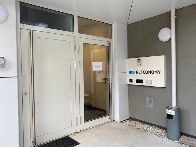 Eingangsbereich eines modernen Geschäftsgebäudes mit Glastüren und Firmenbeschilderung an der Fassade.