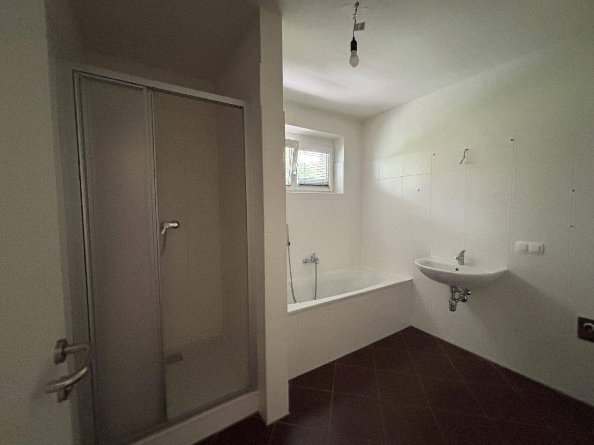 Badezimmer mit Duschkabine, Badewanne, Waschbecken und Fenster für Tageslicht.