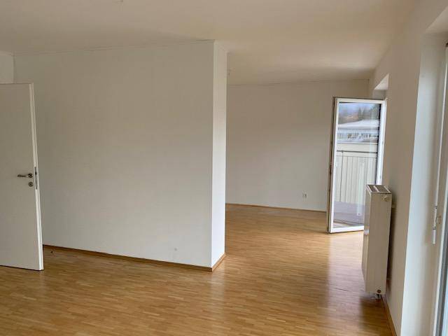 Geräumiger Wohnbereich mit hellem Parkettboden und Zugang zu einem Balkon.