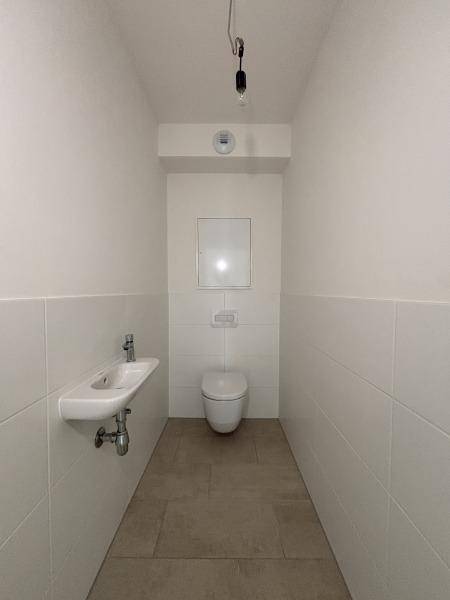 Modernes Gäste-WC mit wandhängender Toilette, kleinem Waschbecken und hellen Fliesen.