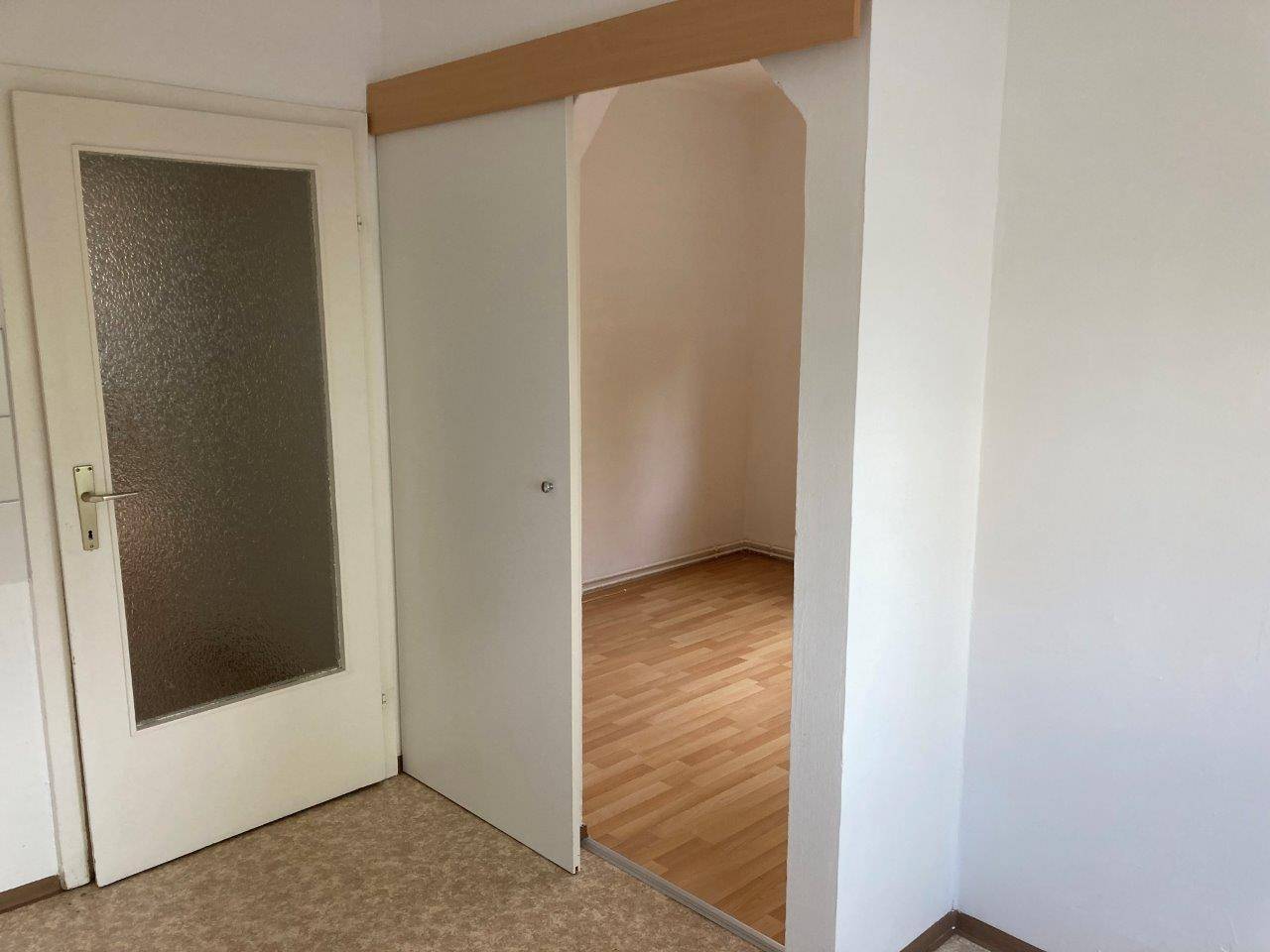 Durchgang zu einem weiteren Zimmer mit Schiebetür und hellem Boden.