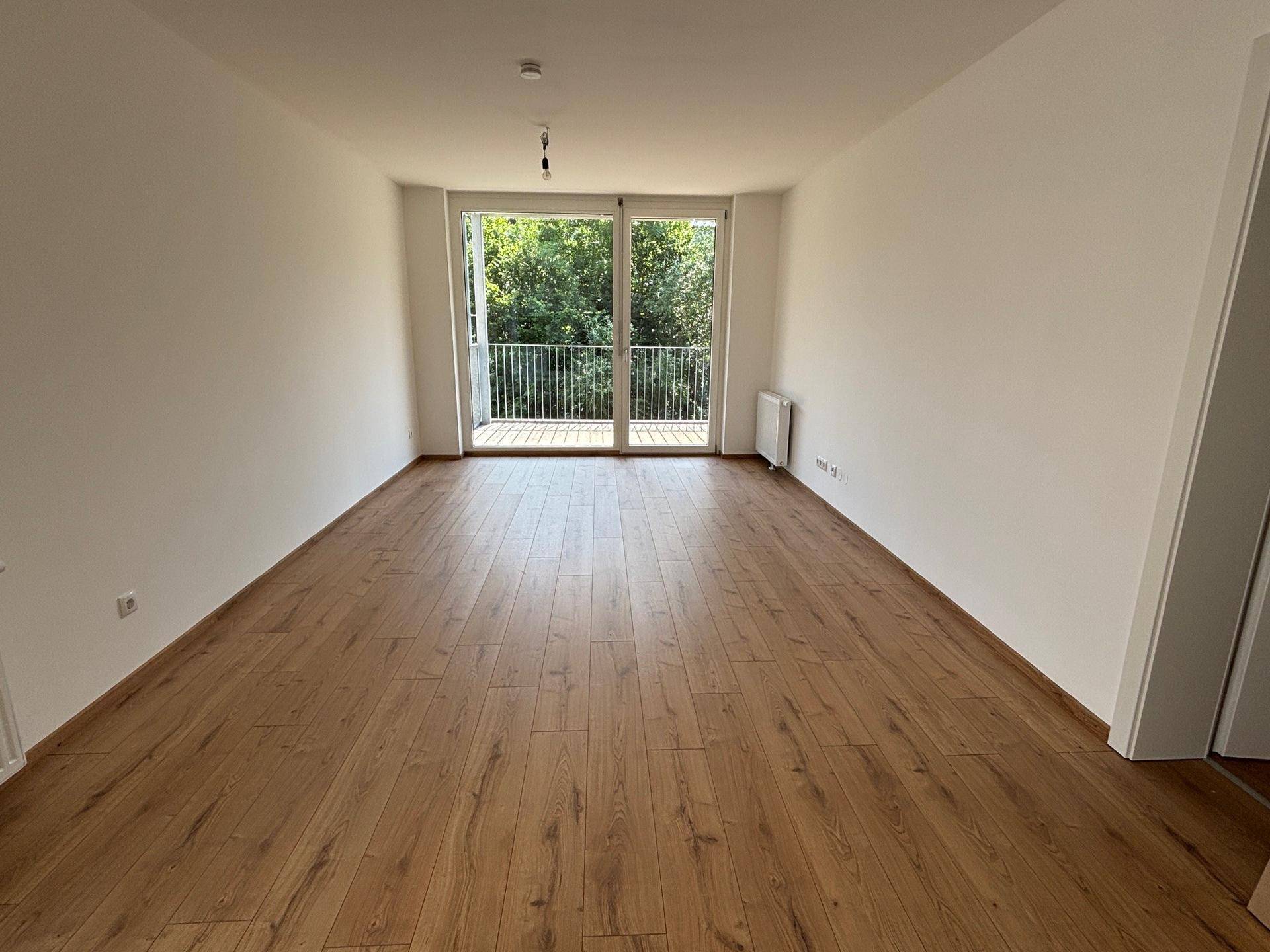 Geräumiges Wohnzimmer mit Laminatboden und großem Balkonzugang, bietet viel Tageslicht.