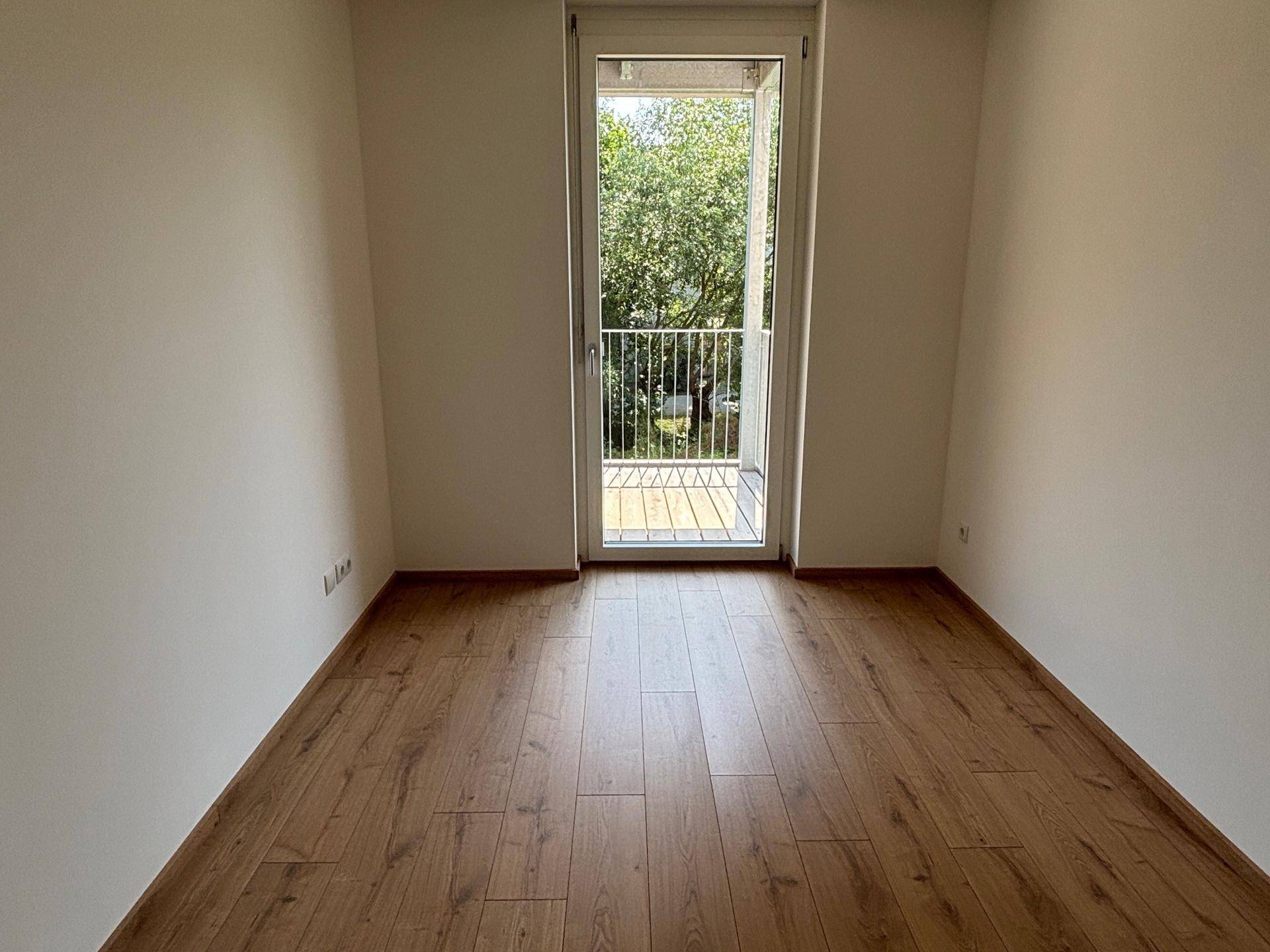 Helles Zimmer mit Laminatboden und Balkonzugang, bietet einen angenehmen Blick ins Grüne.