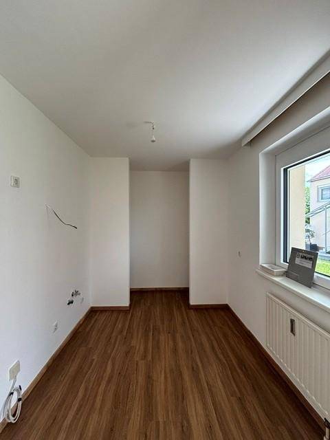 Leeres Zimmer mit Laminatboden, weiß gestrichenen Wänden und einem Fenster für natürliches Licht.