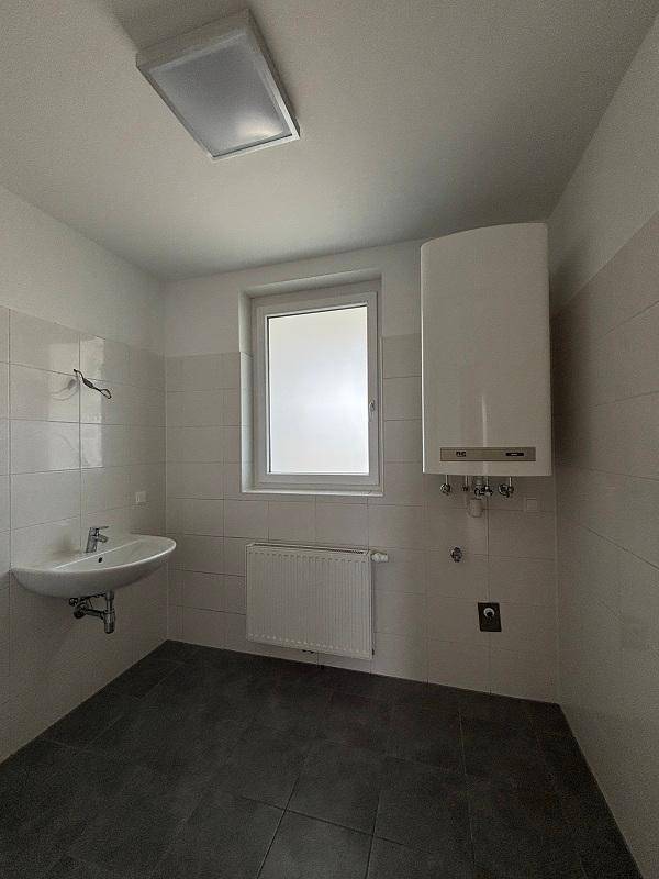 Badezimmer mit Waschbecken, Fenster, Heizkörper und Wandboiler.
