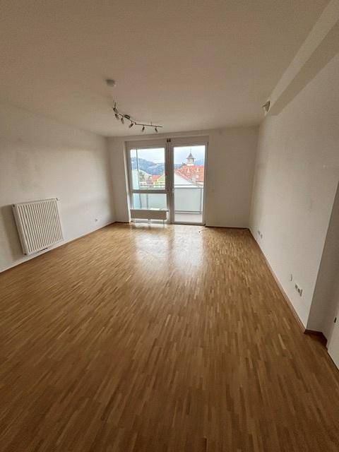 Helles Wohnzimmer mit Parkettboden und Zugang zu einem Balkon, der eine schöne Aussicht bietet.