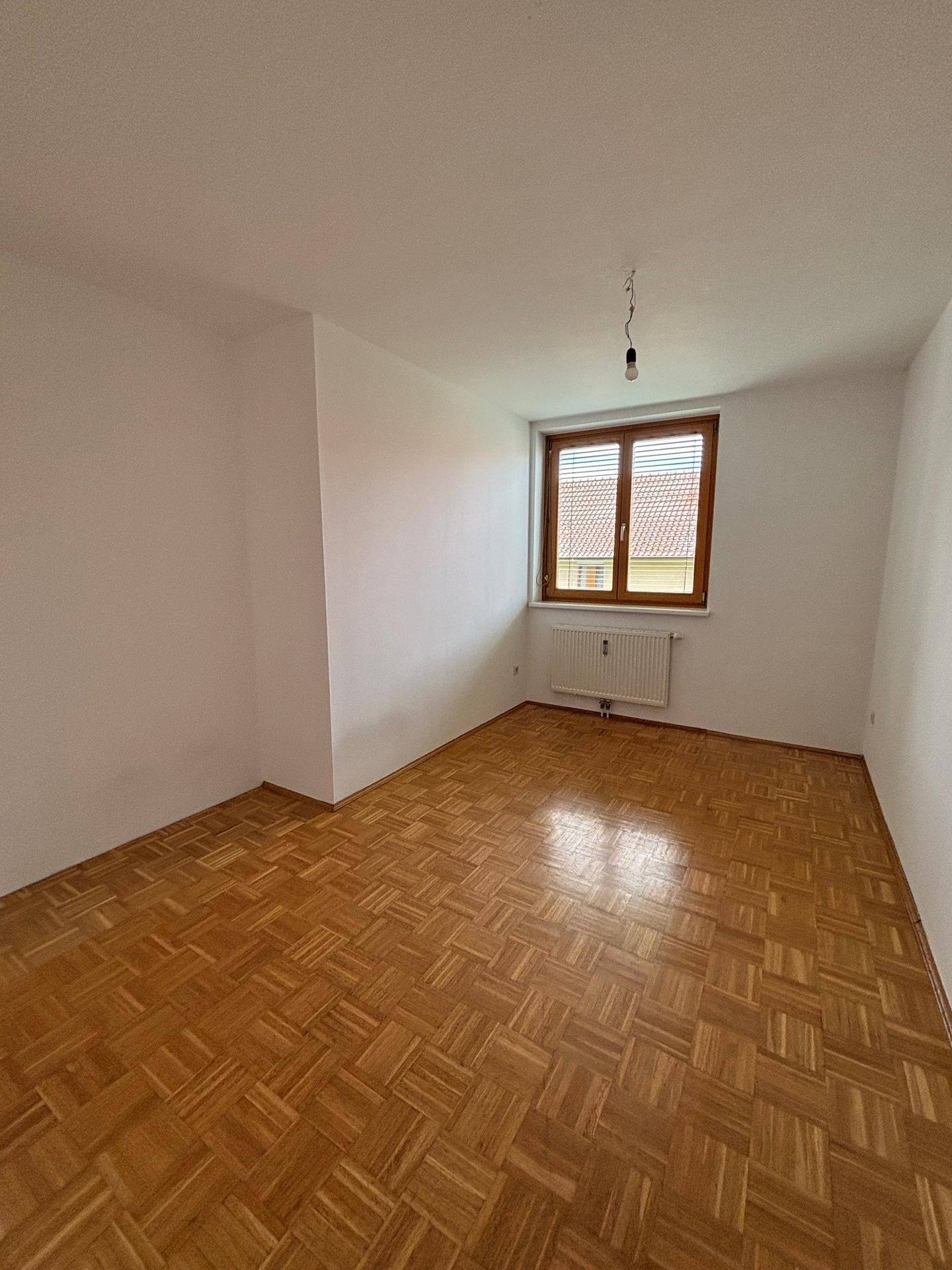 Geräumiges Schlafzimmer mit hellem Parkettboden und viel Tageslicht durch das große Fenster.