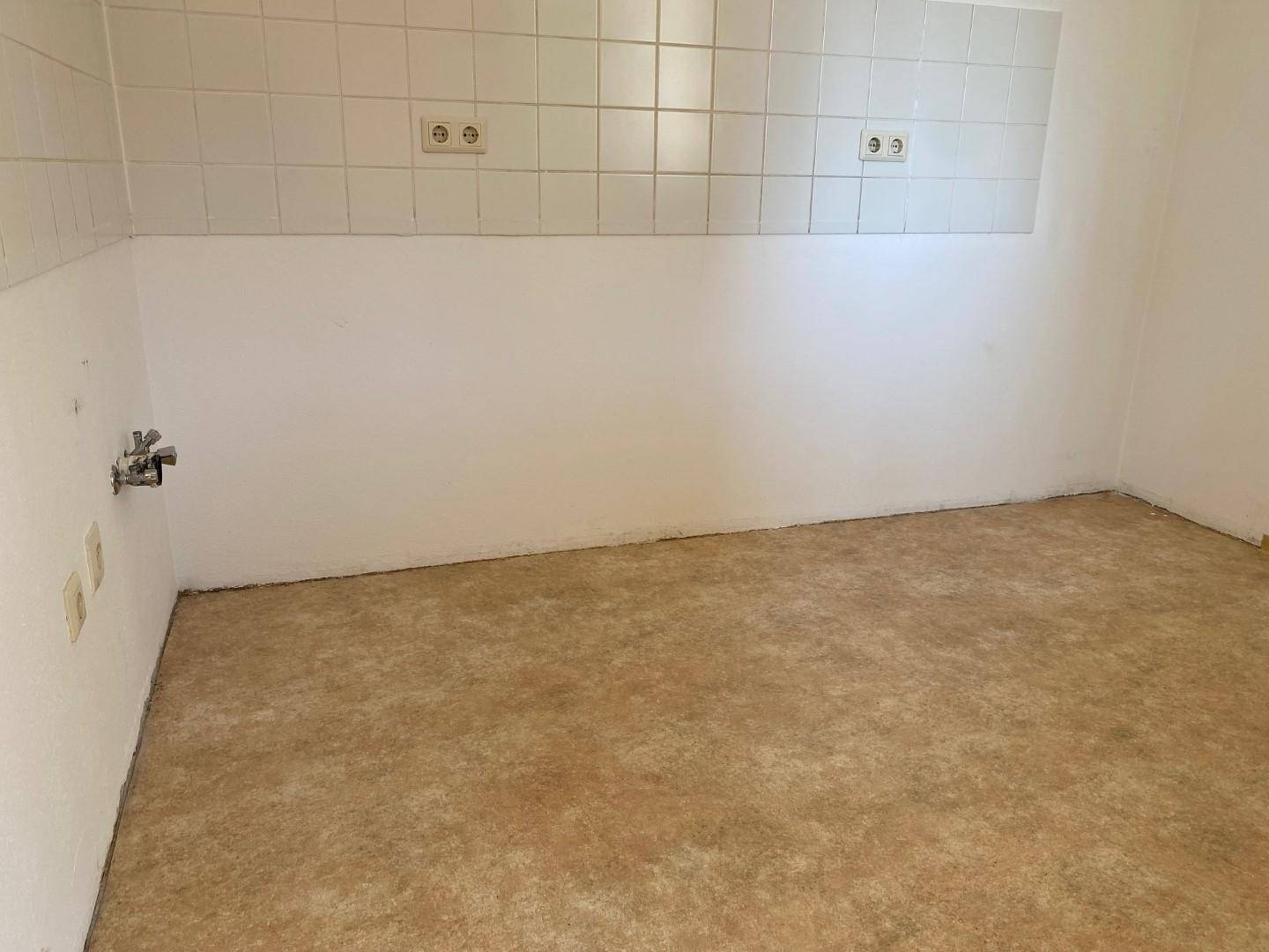 Leerer Küchenraum mit gefliestem Spritzschutz und Linoleumboden, bereit für die Installation einer Küche.
