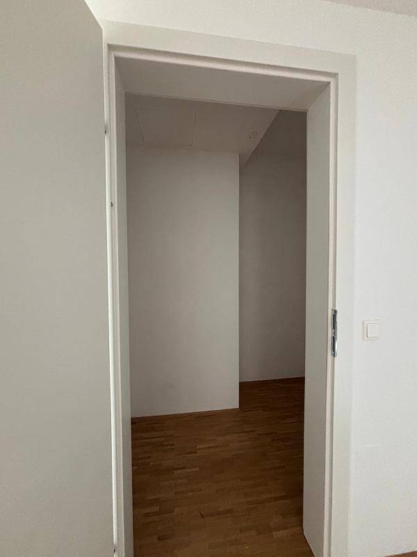 Blick durch eine offene Tür in einen weiteren leeren Raum mit Parkettboden.