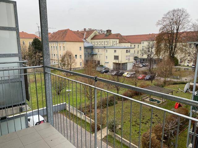 Blick vom Balkon auf eine grüne Wohnanlage mit Spielplatz und umliegenden Gebäuden.