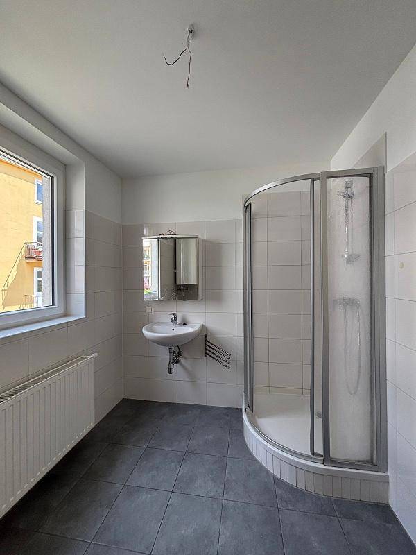Badezimmer mit Duschkabine, Waschbecken, Spiegelschrank und Fenster für natürliche Belüftung und Licht.
