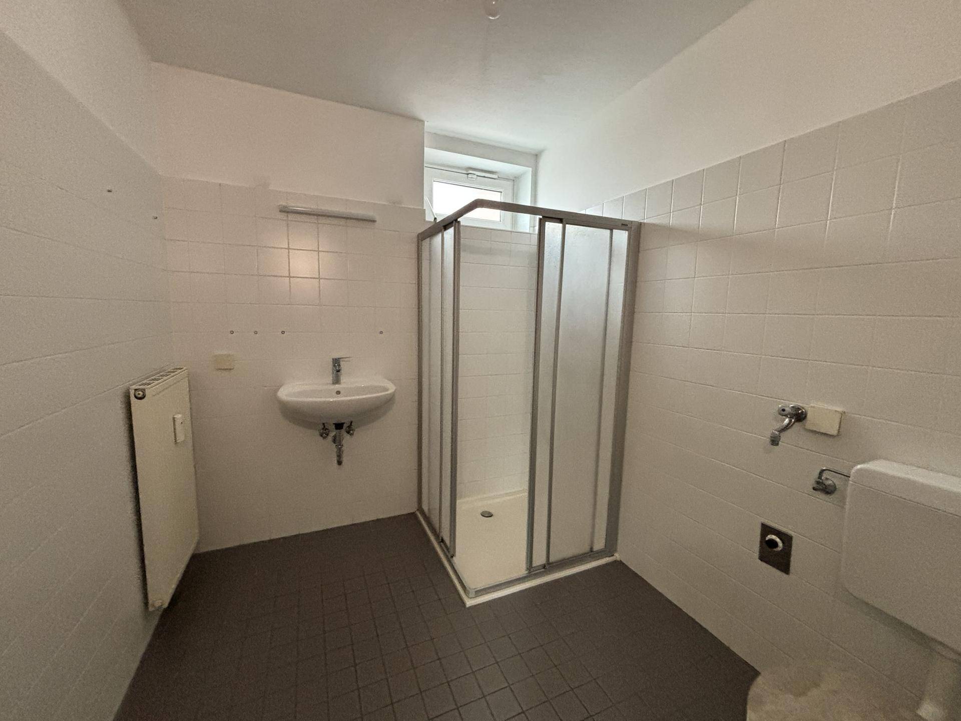 Badezimmer mit Duschkabine, Waschbecken, Toilette und Fenster für Tageslicht.