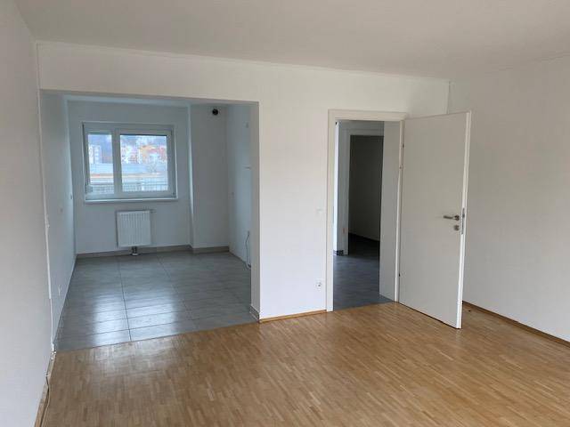 Heller Wohnbereich mit Parkettboden und angrenzendem gefliesten Raum mit Fenster.